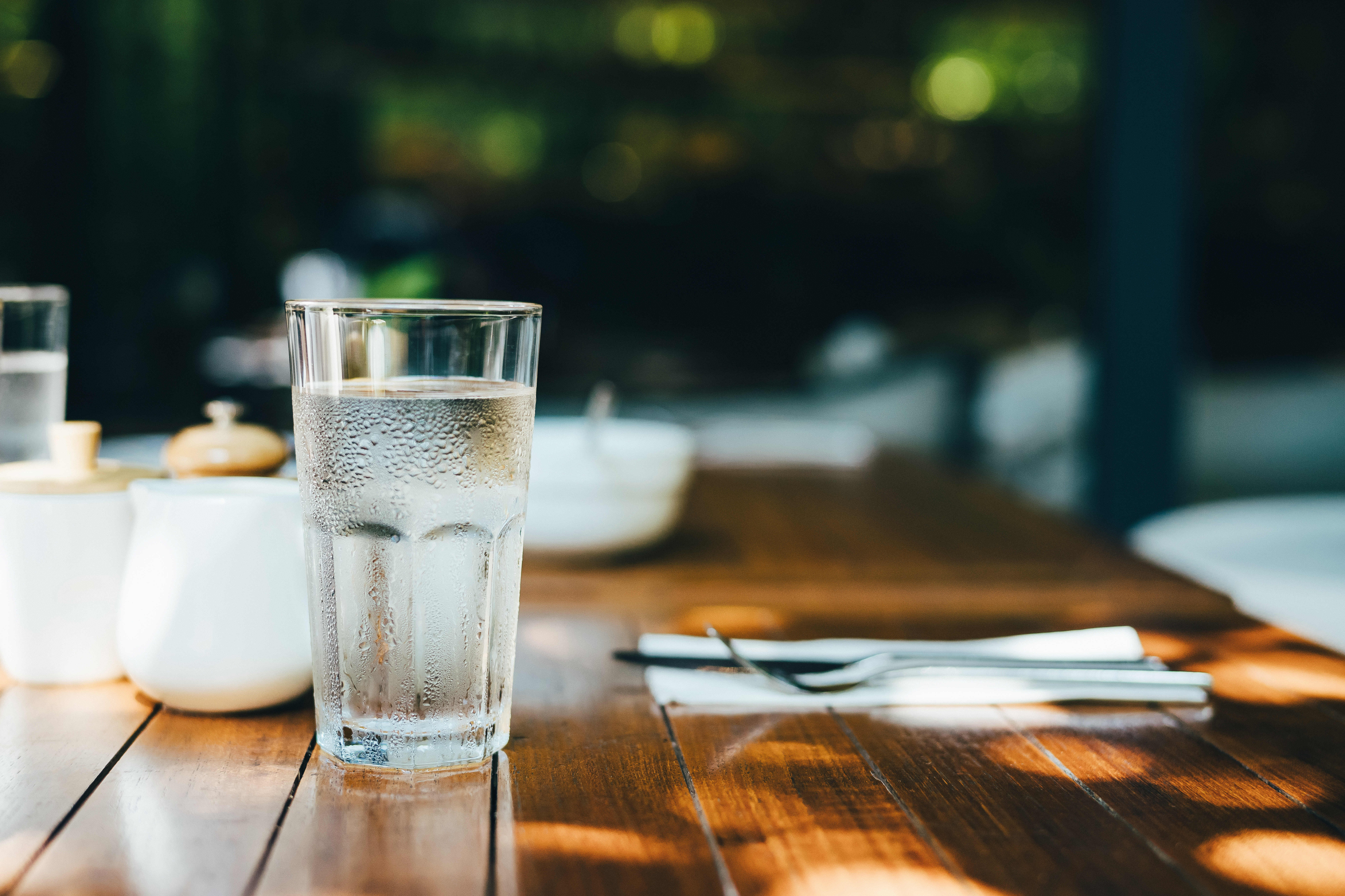 A glass of water served on table in an outdoor restaurant against beautiful sunlight