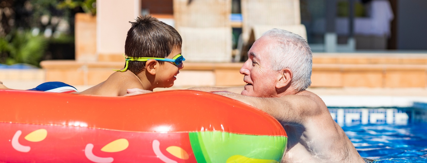 A grandfather talking to his grandson who is floating on an orange pool float.