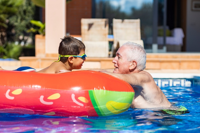 A grandfather talking to his grandson who is floating on an orange pool float.