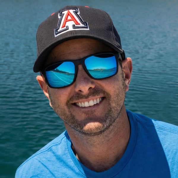 Matthew Horowitz wearing sunglasses, smiling in a blue shirt and black hat with an embroidered A.