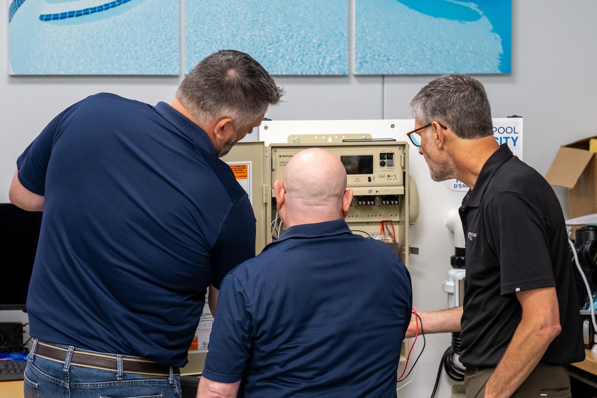 Three men in blue polos and jeans, working on a Pentair IntelliCenter