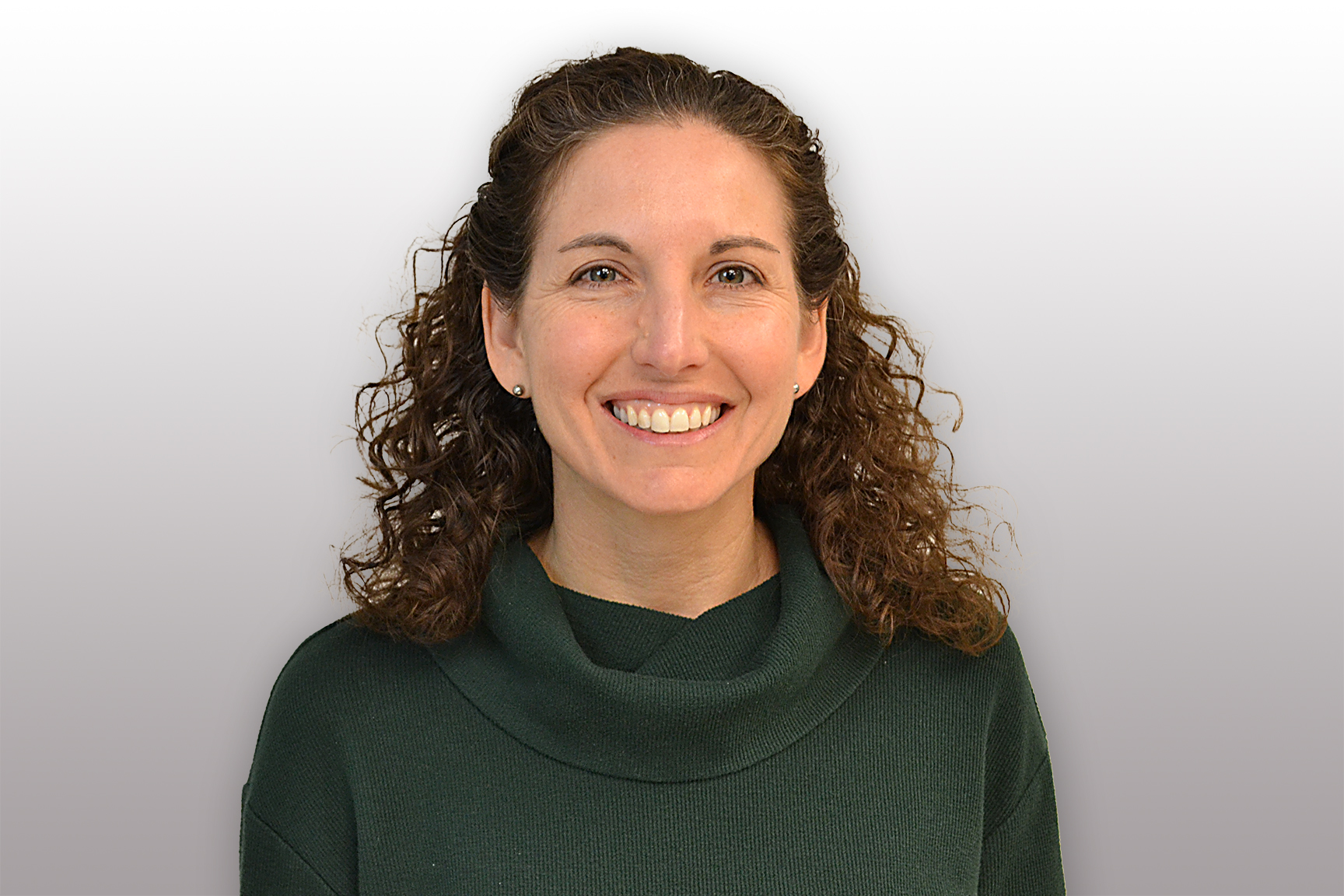 Christine Richardson. A light skinned woman with brown curly hair, wearing a dark turtleneck