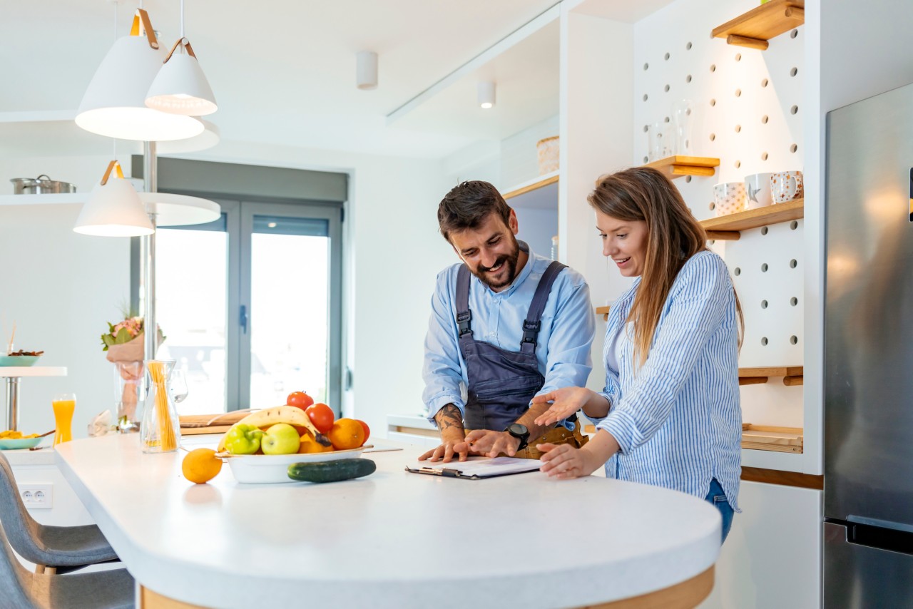 Young professional plumber in blue uniform shows results of work for housewife on the kitchen.