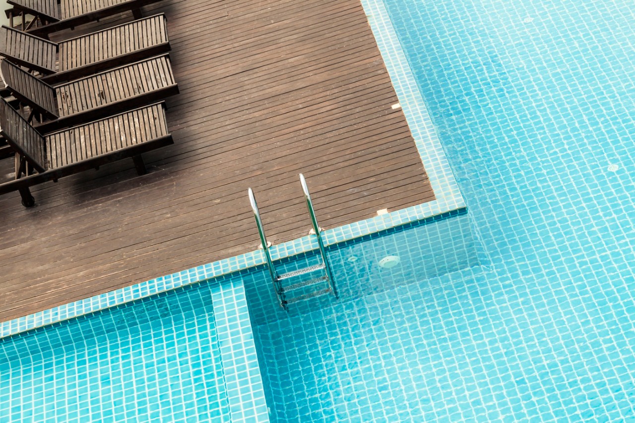 closeup of tiled pool with wooden deck and lounge chairs and pool ladder