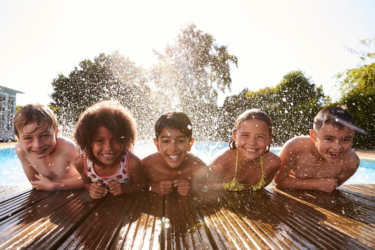multiple children laughing smiling and having fun in outdoor swimming pool with splash of water