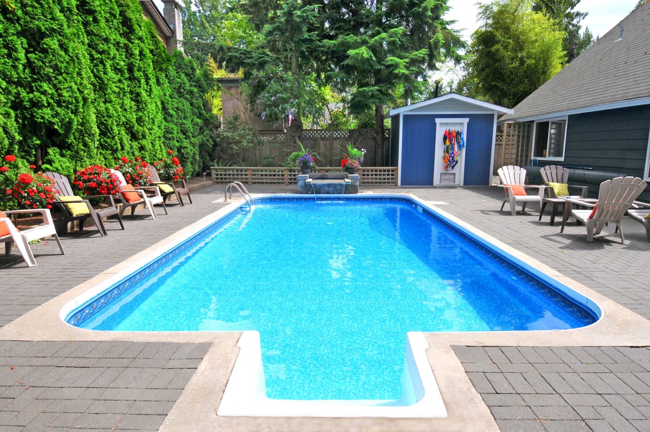 enclosed backyard swimming pool with waterfall and blue pool house green trees and adirondack chairs