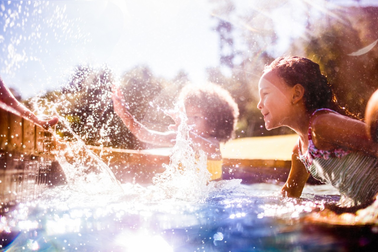 Little girl with her friends splashing happily together in a pool in summer