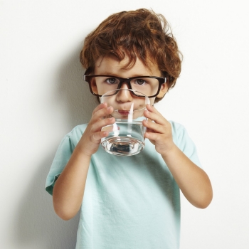 Young boy with glasses drinking a cup of water looking at camera