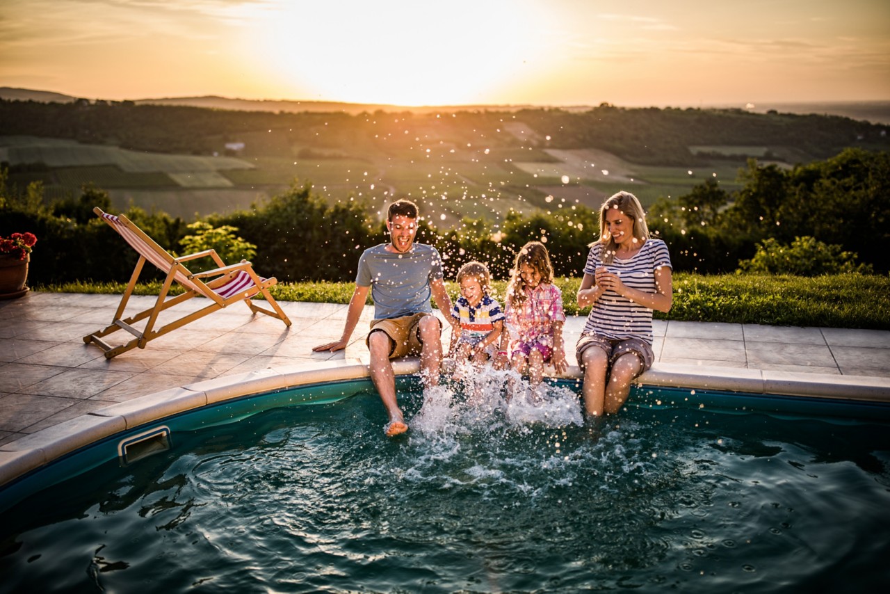 Young happy family having fun while splashing water with their legs in the pool.