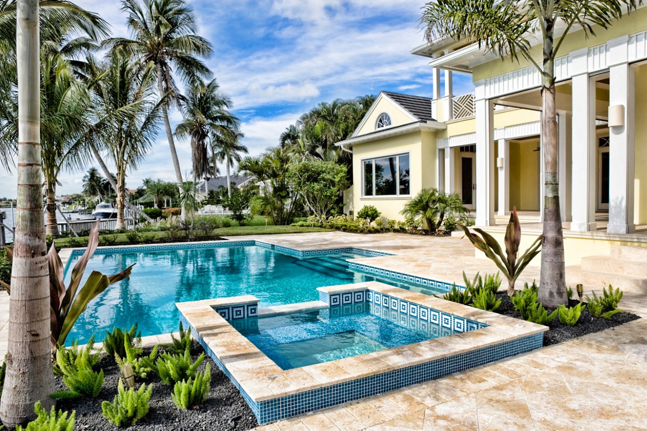 tropical backyard swimming pool and hot tub with yellow home in Florida surrounded by palm trees