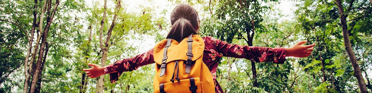 Teen wearing orange backpack with arms wide in nature