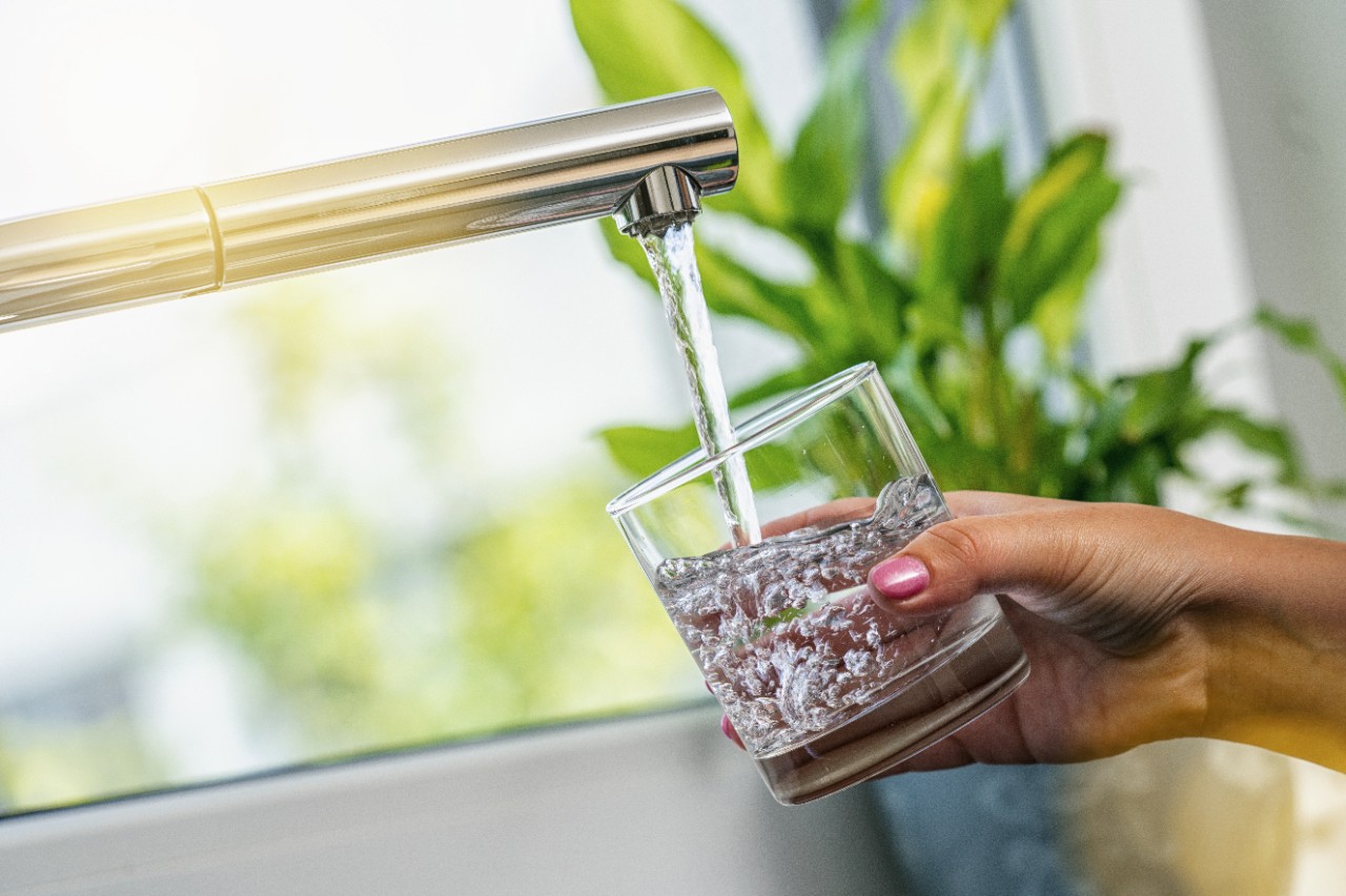 Woman hand holds a glass to fill it with water from kitchen faucet tap; water filtration, drinking water, glass of water 