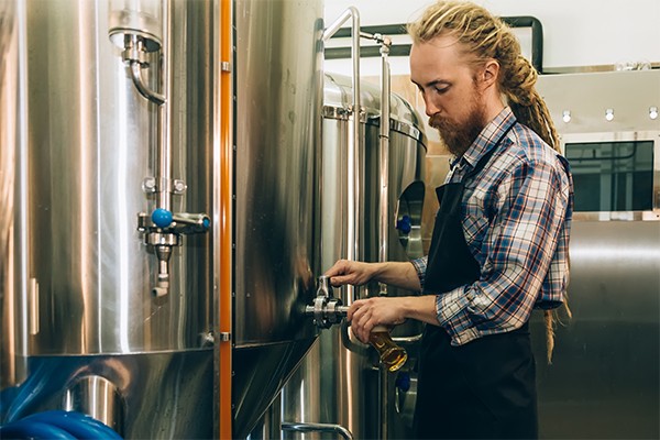 Brewer filling beer in glass from tank at brewery