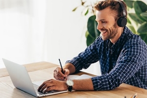 smiling man in headphones taking part in webinar at tabletop with notebook in office; Adobe Stock: 227016314