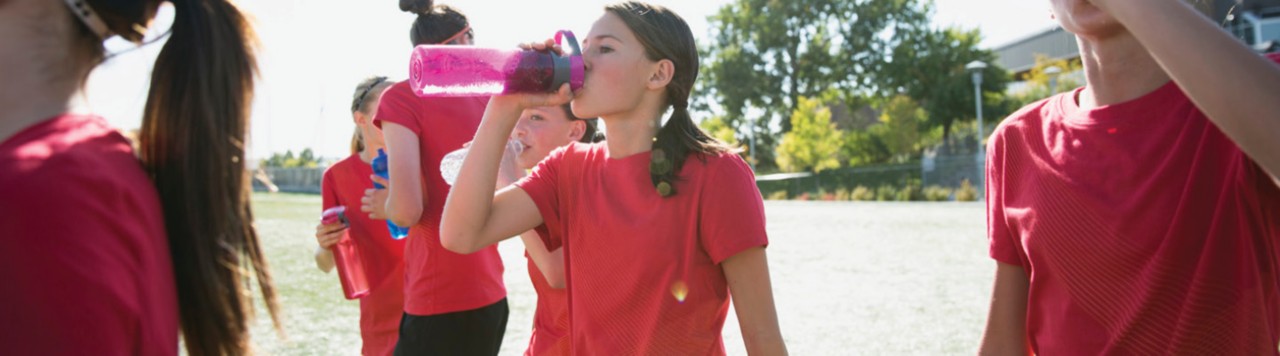 girls in red drinking water outside playing soccer 1400x400