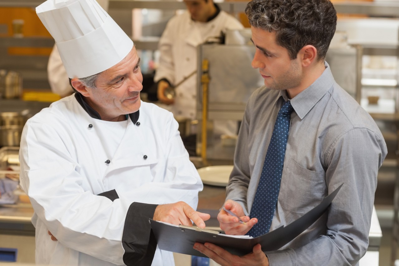 Waiter and chef discussing the menu in the kitchen; Shutterstock ID 139385570