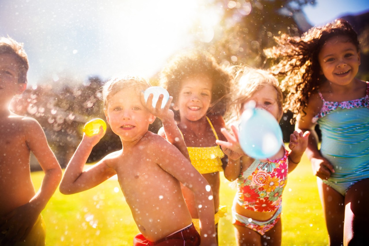 young-smiling-children-in-swimsuits-throwing-water-balloons-outdoor-on-sunny-day-horizontal-5760x3840-image-file-469932508