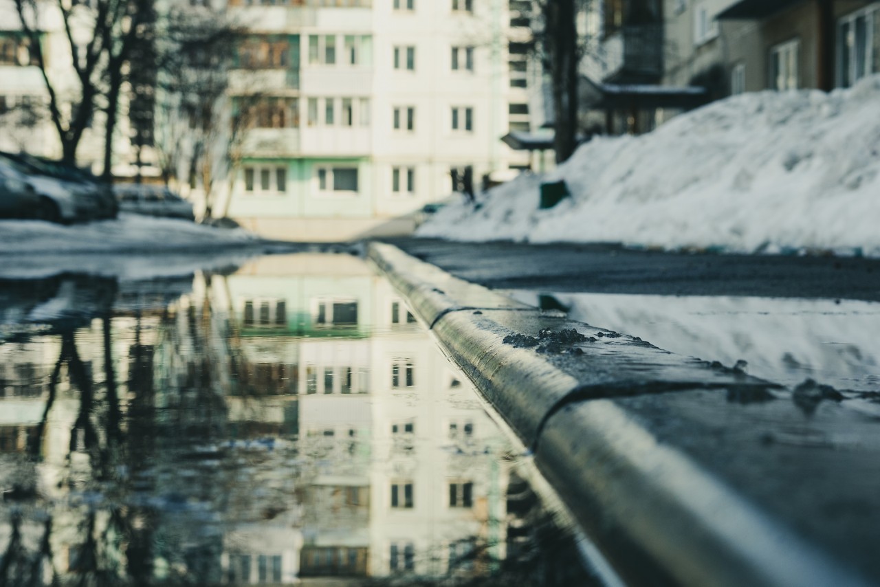 bottom view of the flooded space in front of the house houses and trees reflected in the water, snow and wet asphalt in the background