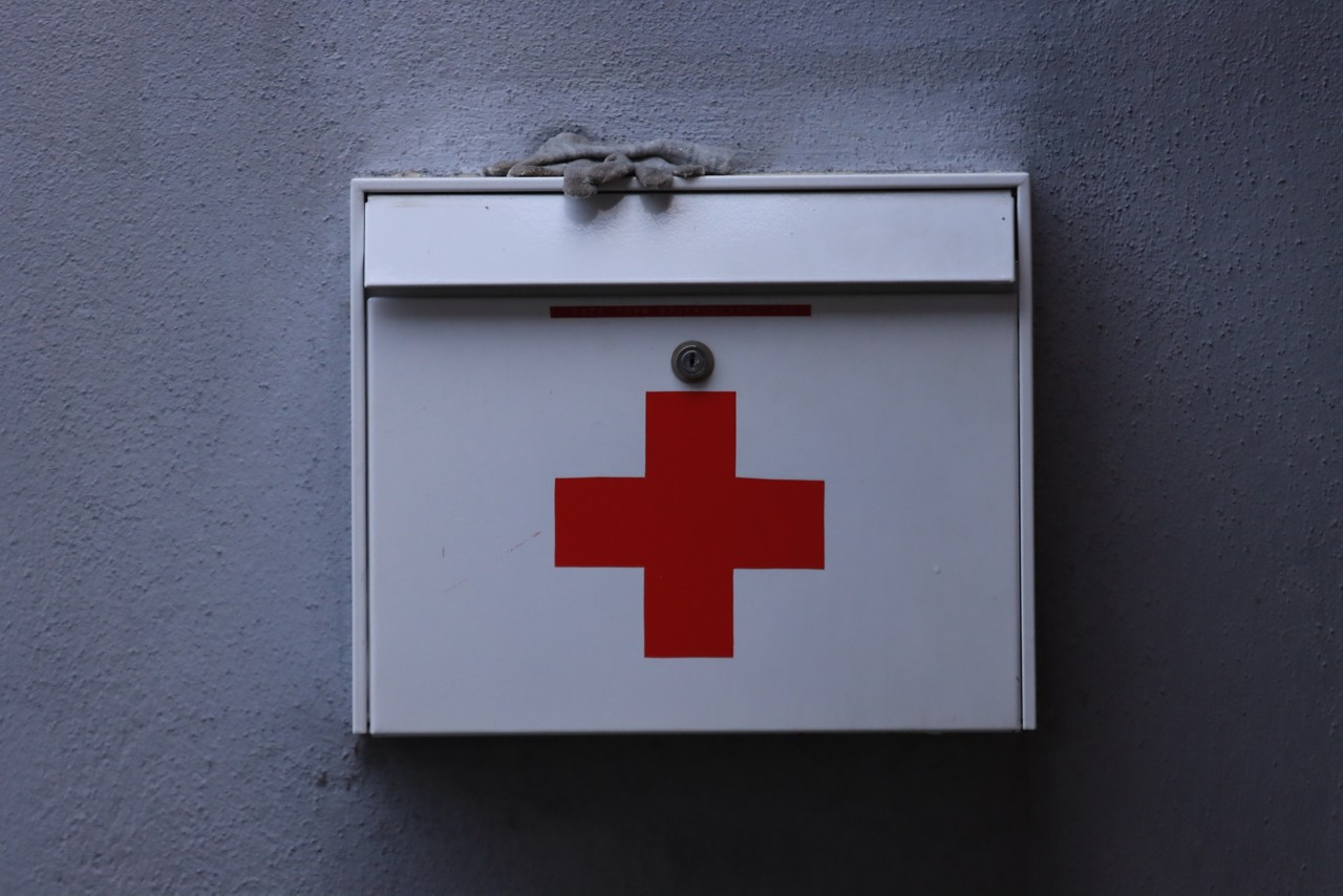 White first aid kit with a red cross mounted on a wall at a pool