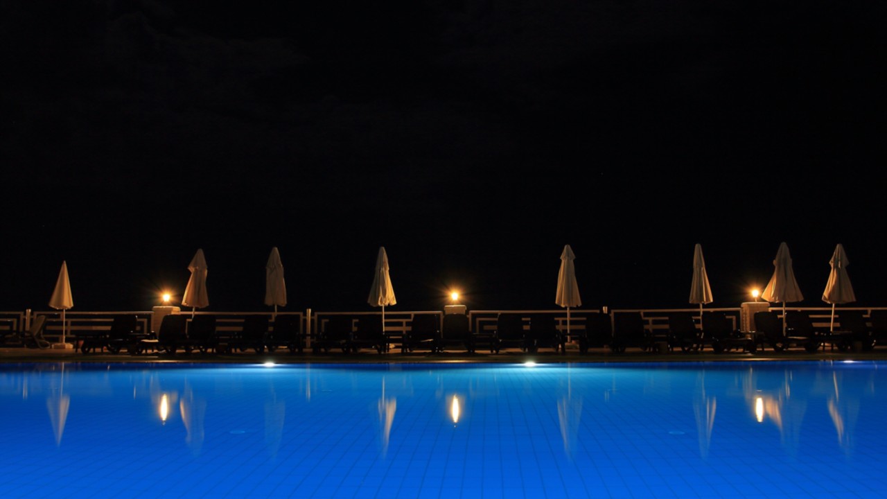 illuminated outdoor swimming pool at night with closed beach chair umbrellas