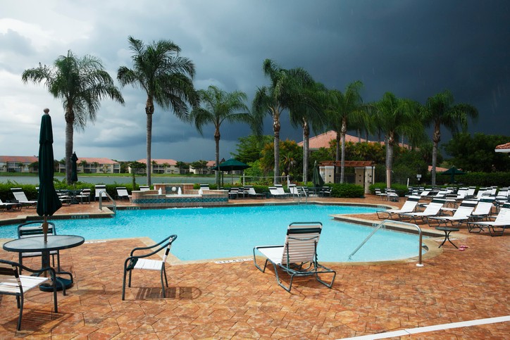 Dark tormy skies are coming in over a palm tree surrounded freeform pool.