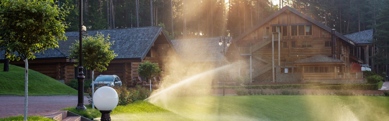 Watering the lawn near wooden house  on a summer morning