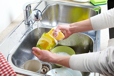 Hands washing dishes with running water from faucet in sink