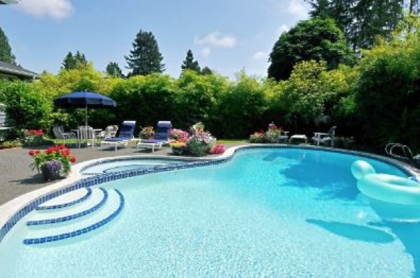 A kidney shaped pool with clear blue water surrounded by pool furniture on a bright sunny day. 