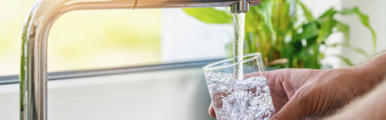 person filling water glass at faucet