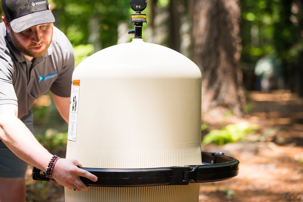 A man is securely lifitng the arms of a filter clamp while lifting it over the filter.