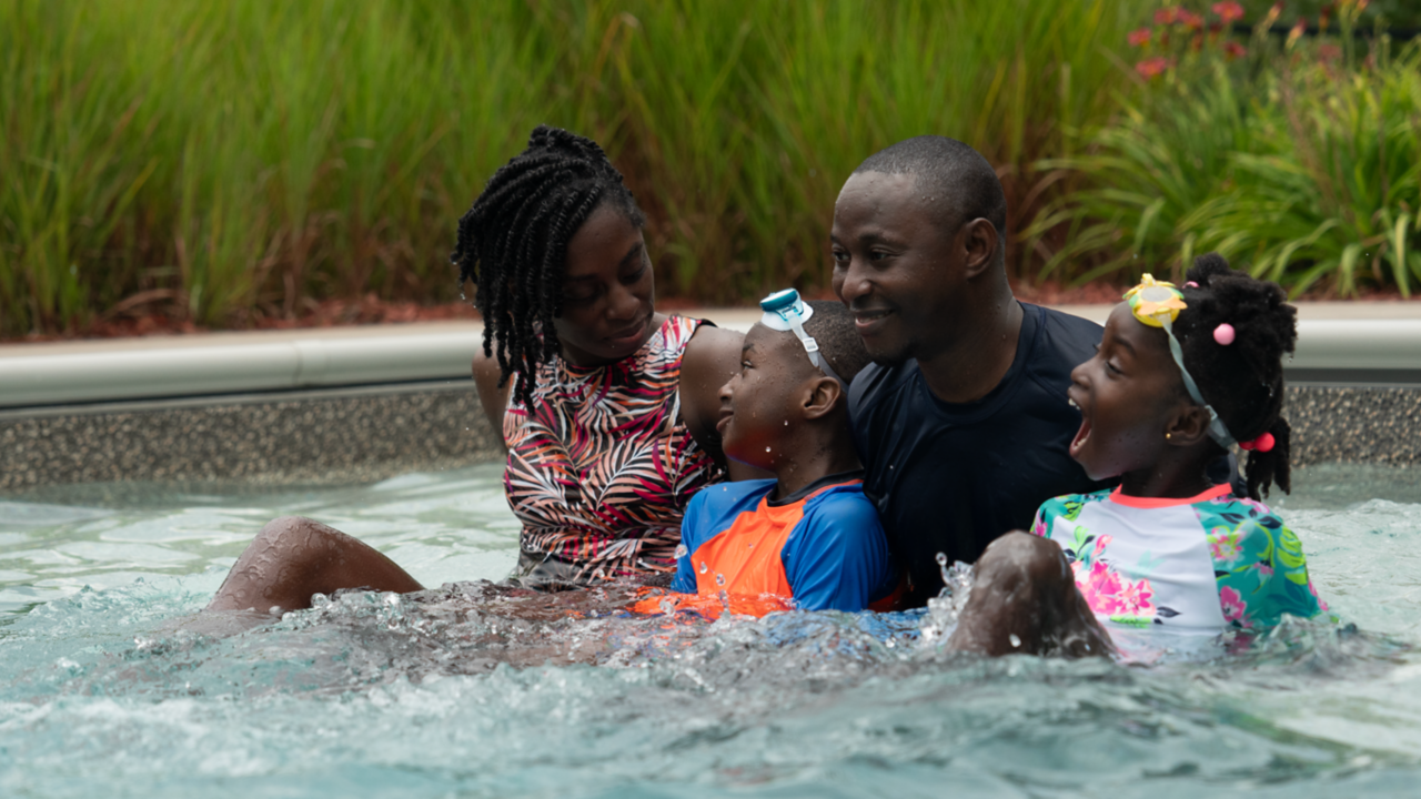 A young black family of four relaxing and smiling in a pool.