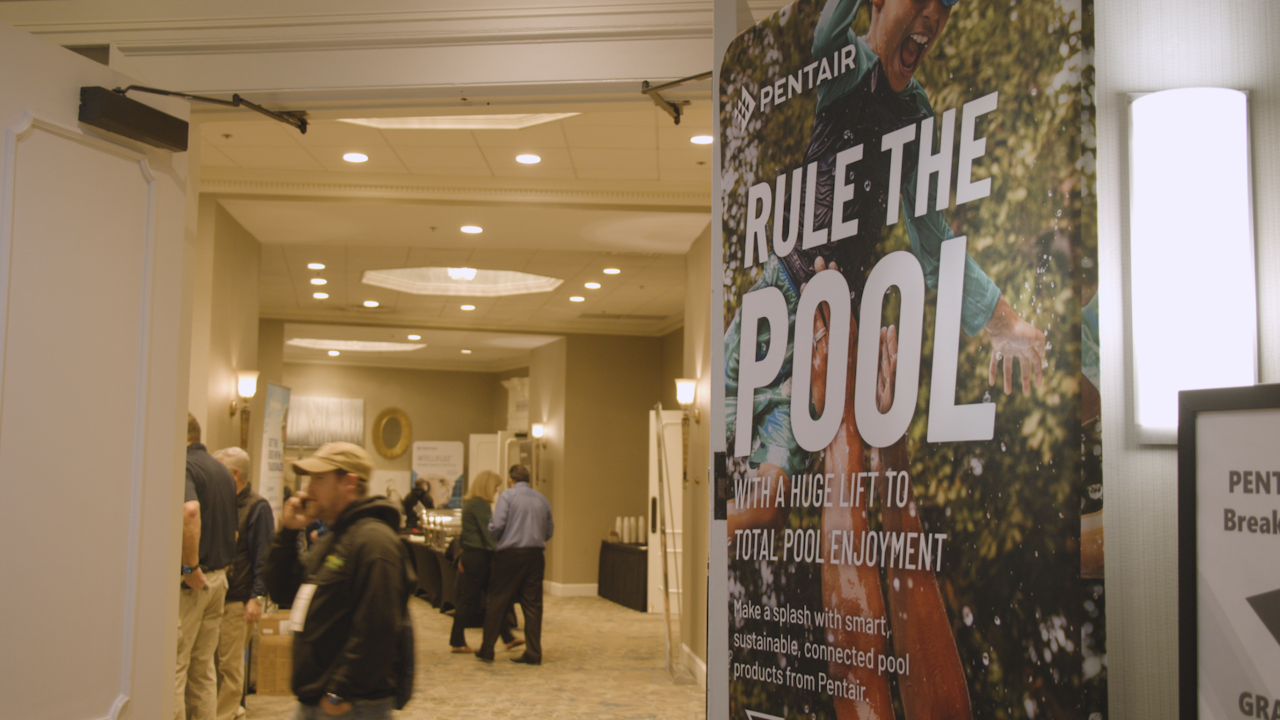 A group of people standing in a hallway with a sign on the right "Rule the Pool"