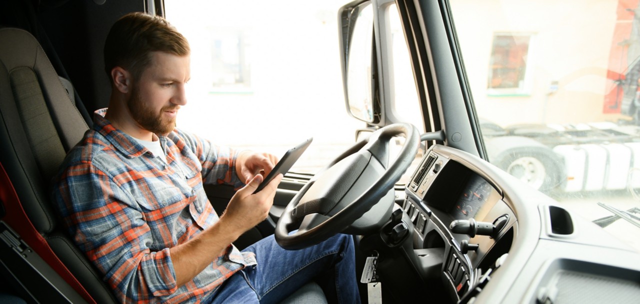 Man truck driver sitting behind wheel of car and holding digital tablet in his hands.