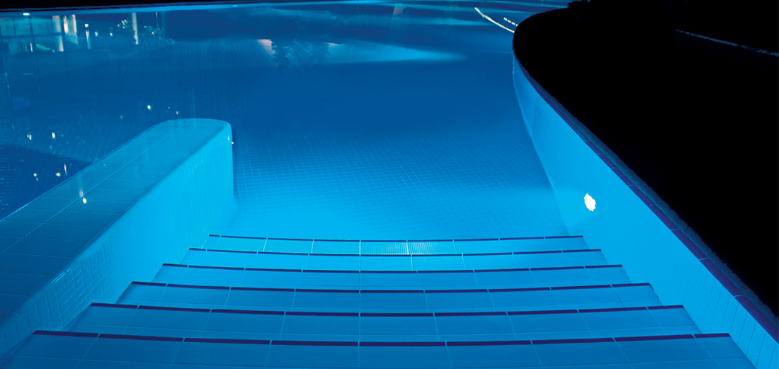 The entrance steps to a pool at night are illuminated.