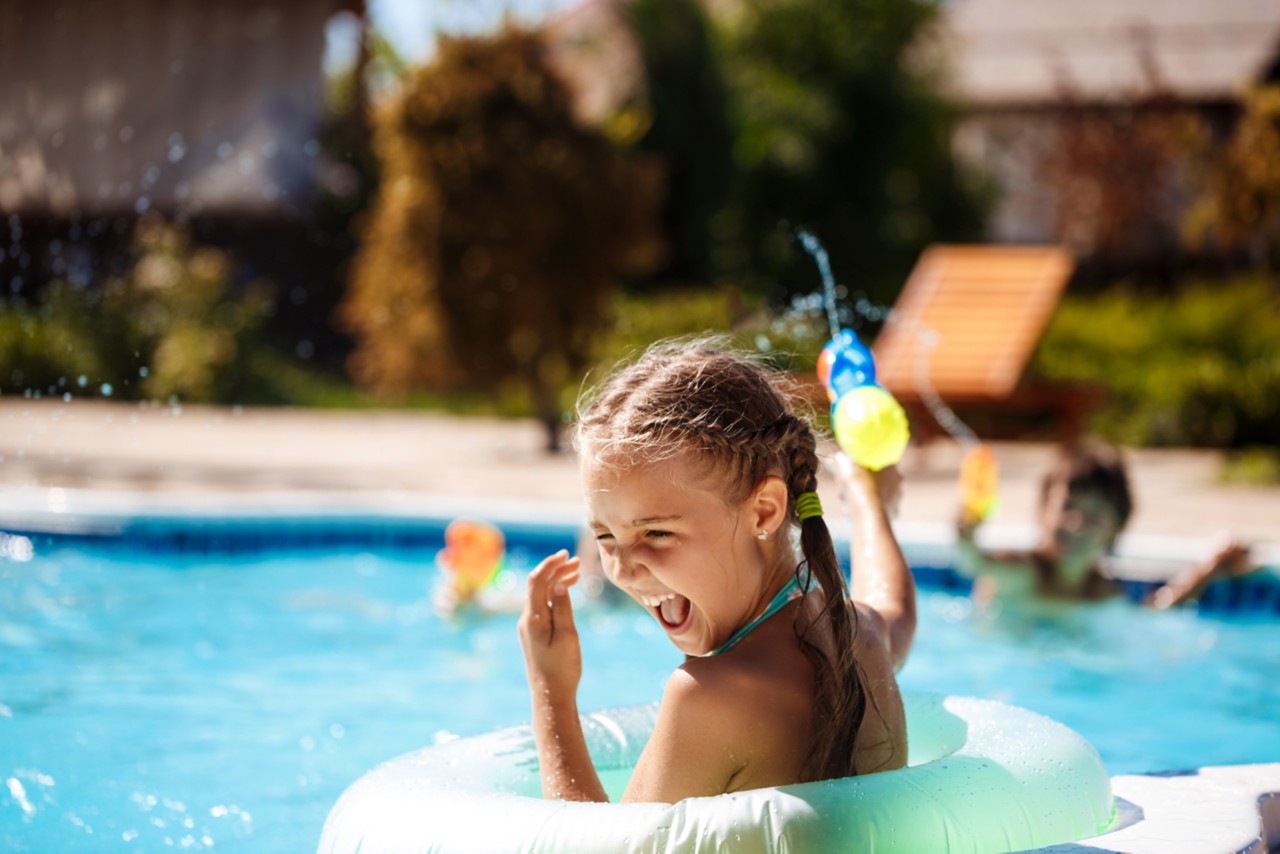 A little boy and girl playing in a pool with waterguns.