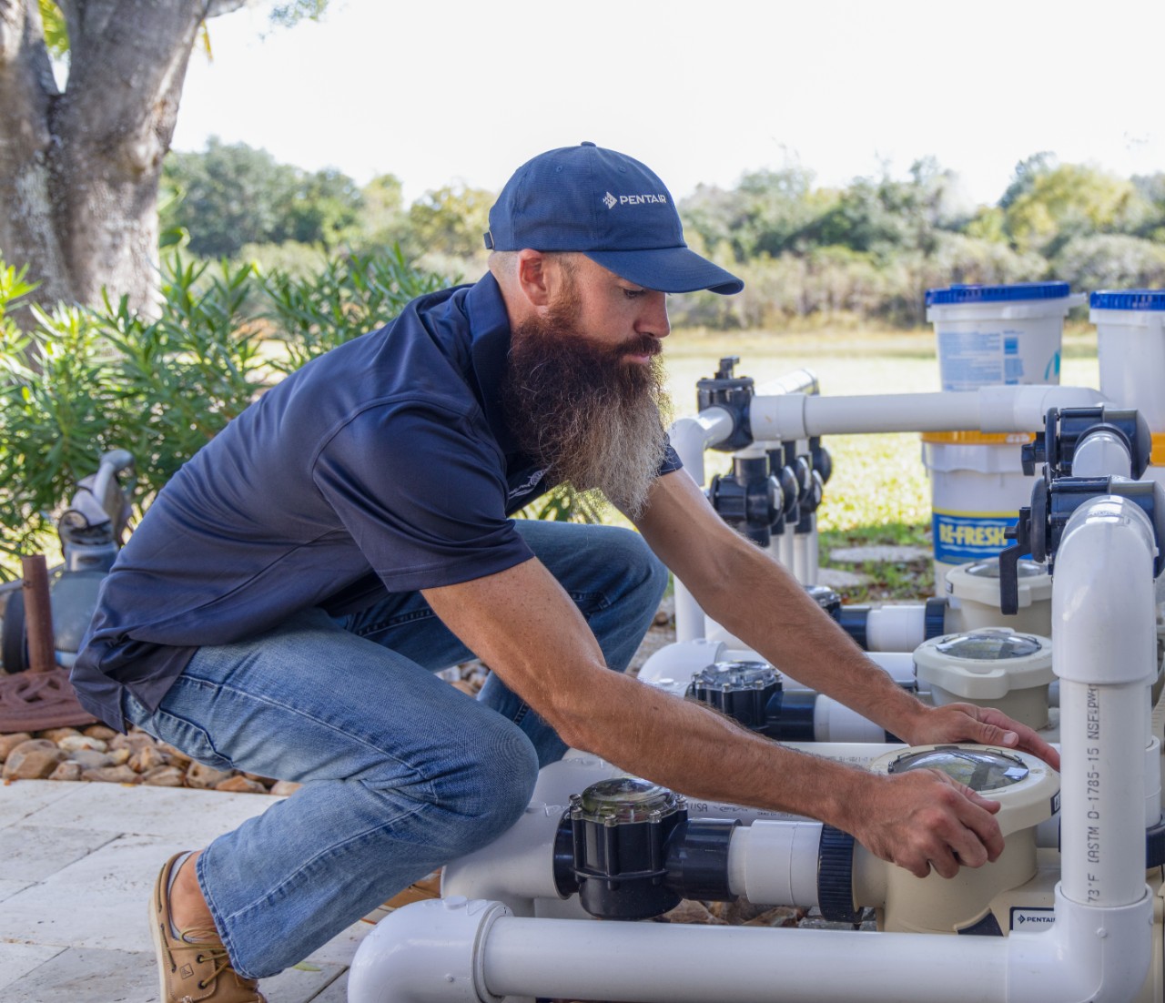 A pool professional in blue, wearing a pentair hat, is working on a Variable Speed Pump.