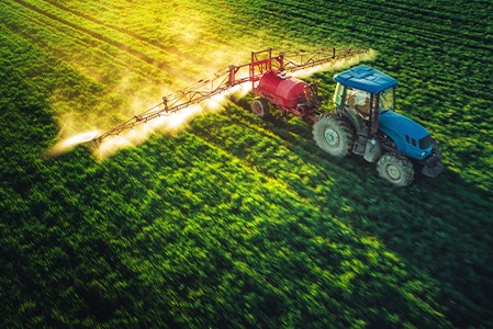 An aerial view of a farming tractor plowing and spraying on a field