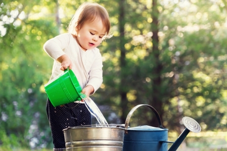 Happy toddler girl playing with watering cans outside