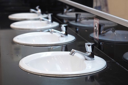 A black countertop with a row of white sinks in a public restroom.