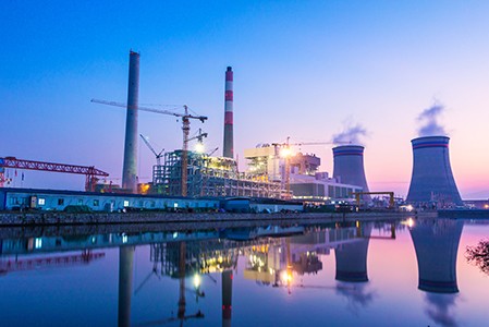 A power plant with a calm body of water in front of a blue and pink sunset.