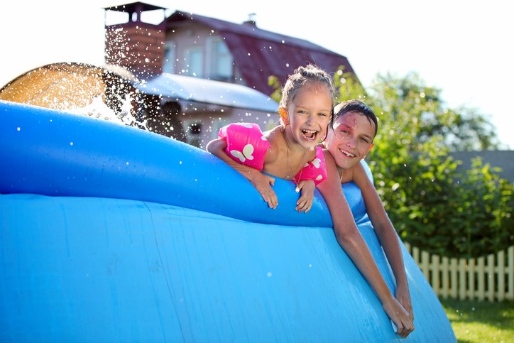 Joyful Caucasian siblings swimming in a inflatable swimming pool and looking at the camera