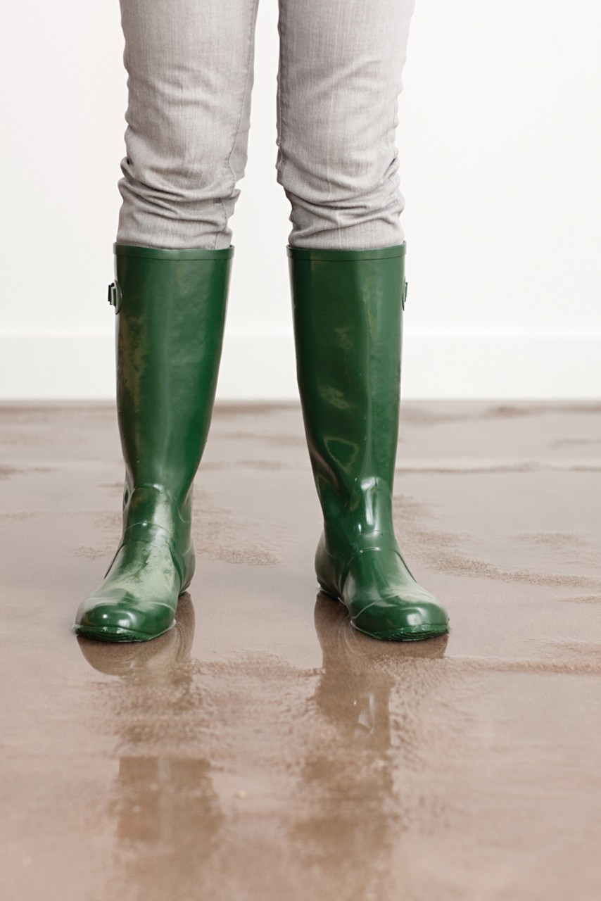 Green rain boots standing on flooded brown carpet