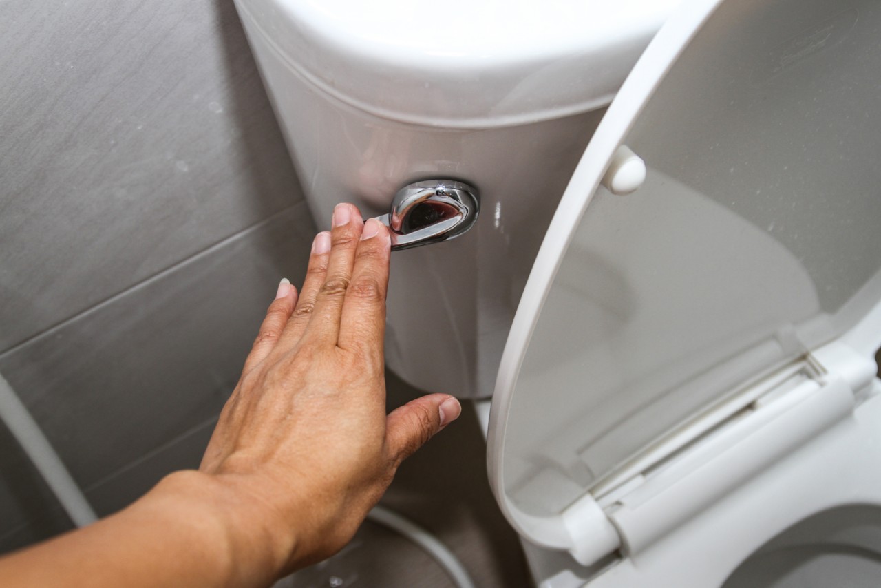 A woman hand pressing a white toilet bowl or flush toilet in the bathroom.