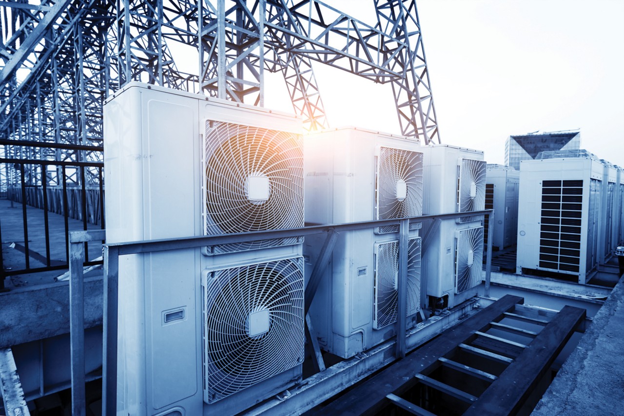 Air conditioner units (HVAC) on a roof of industrial building with blue sky and clouds in the background.