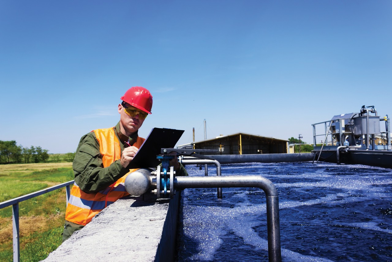 A man in a red helmet and safety vest examining pipes for water treatment.