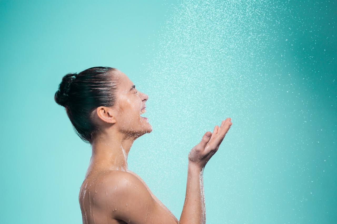 Woman enjoying the water in the shower under a water jet on blue background