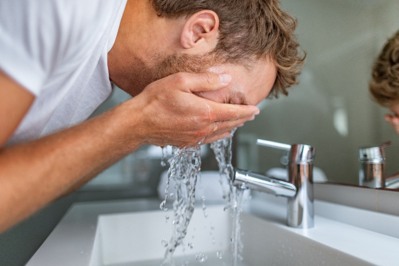 Man in bathroom wash fashsplashing cold water onto face. Water softening, water filtration.