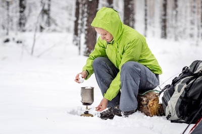 Happy woman cooking near winter tent camp in the snow forest. Bushcraft, survival and people concept; Shutterstock ID 1076679137; purchase_order: pws blog; job: 