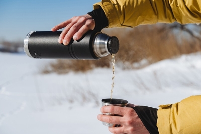Pour the tea from the thermos into a mug. Water flows, pour a hot drink against the background of snow. Black metal thermos, flask for drinks. High quality photo purchase_order: pws blog;