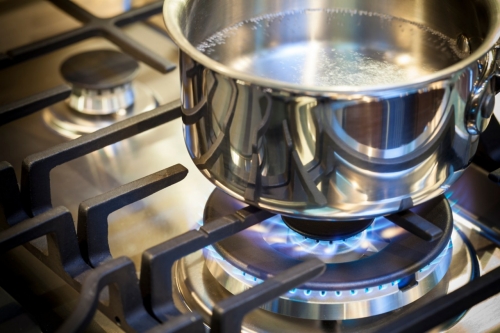 Gas burner on stove with flame on stainless steel surface showing heat ready for cooking food. Stainless steal pot on burner cooking food.
